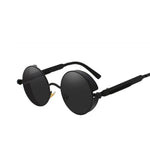 Stylish sunglasses with a black lens and a black rounded frame. The edges of the frames are extended by a small stylish bezel to cover the top and bottom of the eyes. With a spring attached across to the lower part of the handles.