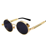 Stylish sunglasses with a black lens and a gold rounded frame. The edges of the frames are extended by a small stylish bezel to cover the top and bottom of the eyes. With a spring attached across to the lower part of the handles.