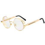 Stylish sunglasses with a clear transparent lens and a gold rounded frame. The edges of the frames are extended by a small stylish bezel to cover the top and bottom of the eyes. With a spring attached across to the lower part of the handles.