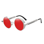 Stylish sunglasses with a red lens and a silver rounded frame. The edges of the frames are extended by a small stylish bezel to cover the top and bottom of the eyes. With a spring attached across to the lower part of the handles.